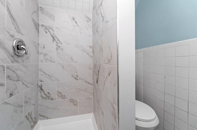 bathroom with tiled shower, tile walls, and toilet