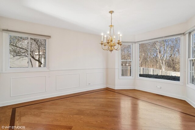 unfurnished dining area featuring an inviting chandelier, a wealth of natural light, and hardwood / wood-style floors