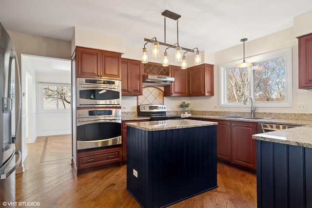 kitchen with appliances with stainless steel finishes, a center island, decorative light fixtures, dark wood-type flooring, and sink