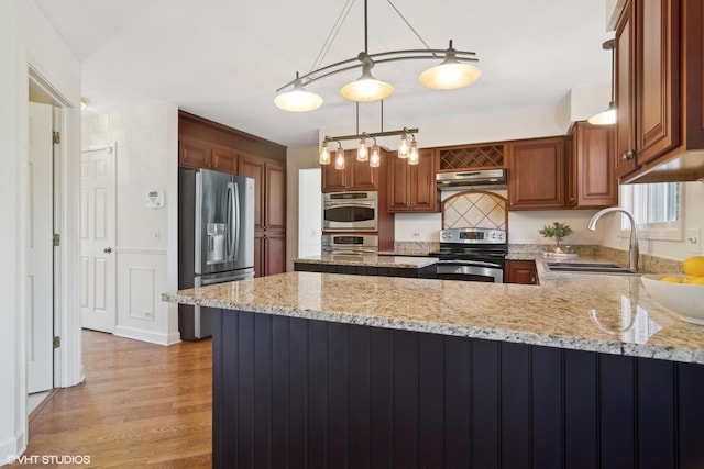 kitchen with appliances with stainless steel finishes, pendant lighting, light stone counters, and sink