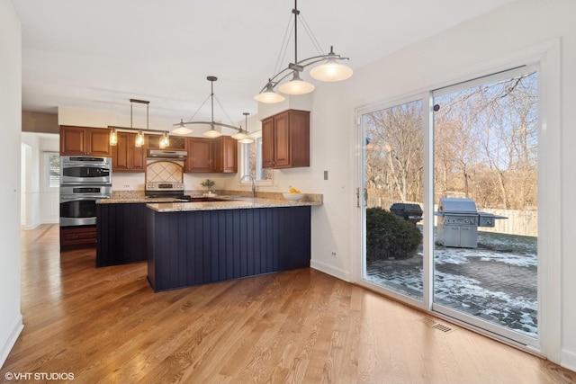 kitchen with light hardwood / wood-style floors, kitchen peninsula, hanging light fixtures, appliances with stainless steel finishes, and light stone countertops