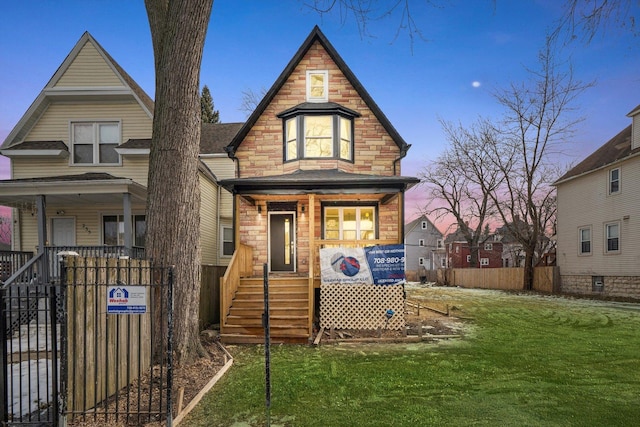 back of property featuring stone siding, covered porch, fence, and a lawn