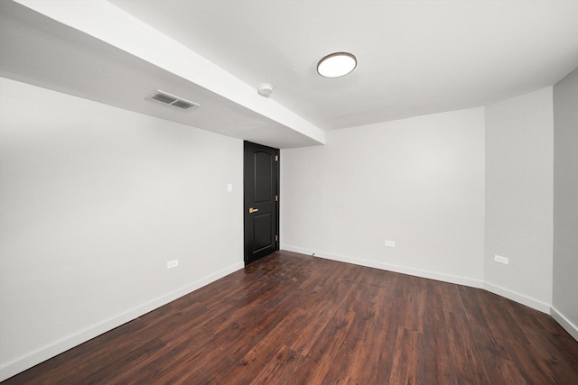 empty room with dark wood-style floors, visible vents, and baseboards