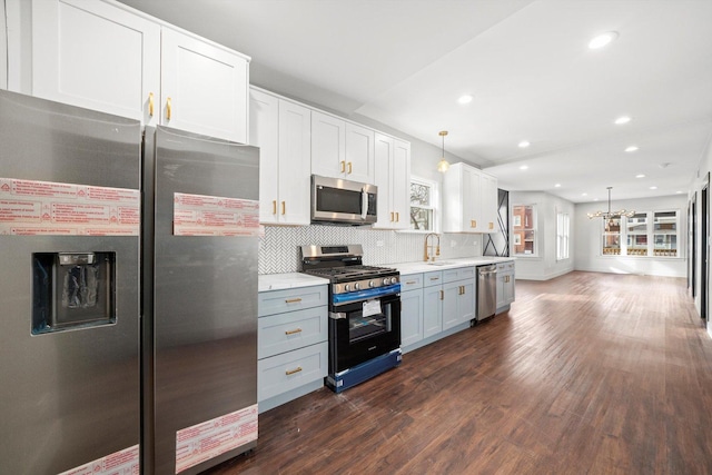 kitchen featuring dark wood-type flooring, a sink, hanging light fixtures, appliances with stainless steel finishes, and decorative backsplash