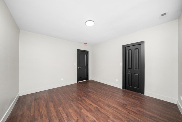 spare room with dark wood finished floors, visible vents, and baseboards