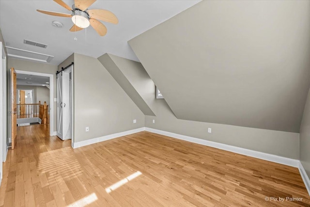 additional living space with ceiling fan, a barn door, lofted ceiling, and light hardwood / wood-style flooring