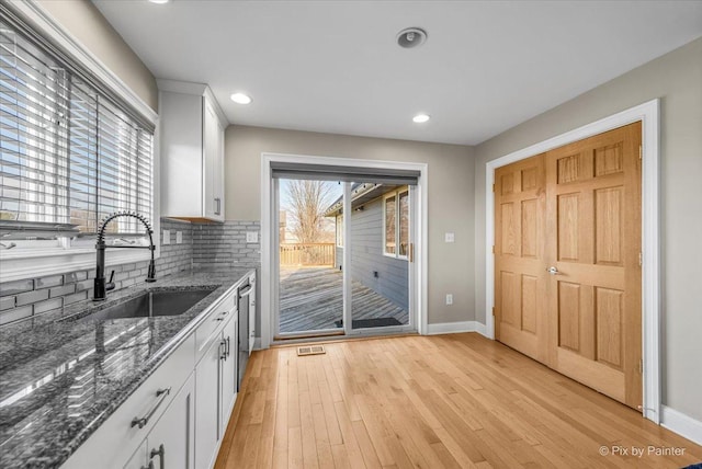 kitchen featuring white cabinetry, sink, stainless steel dishwasher, dark stone countertops, and light wood-type flooring