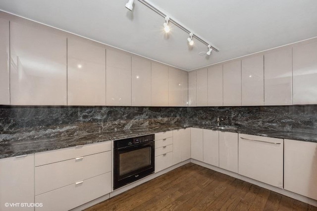 kitchen featuring dark wood-type flooring, dark stone counters, decorative backsplash, black oven, and white cabinetry