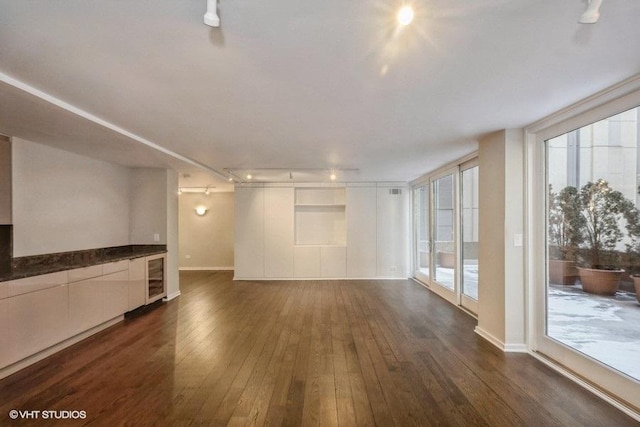 unfurnished living room with rail lighting, wine cooler, and dark wood-type flooring