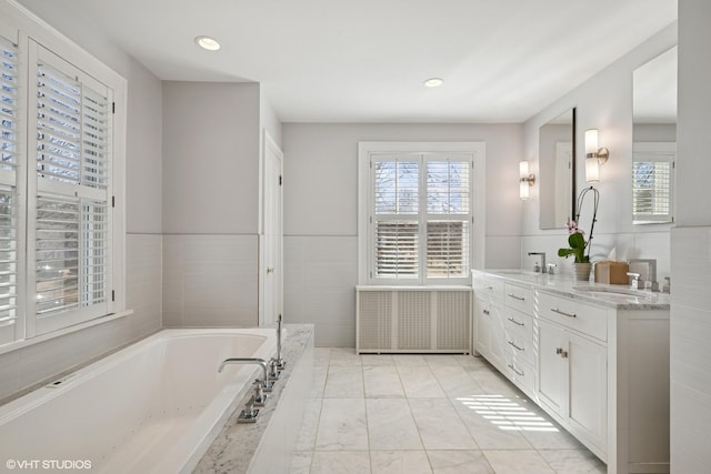 full bath featuring a wainscoted wall, a sink, tile walls, a bath, and double vanity