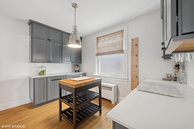 kitchen featuring pendant lighting, radiator, gray cabinetry, light wood-style floors, and baseboards