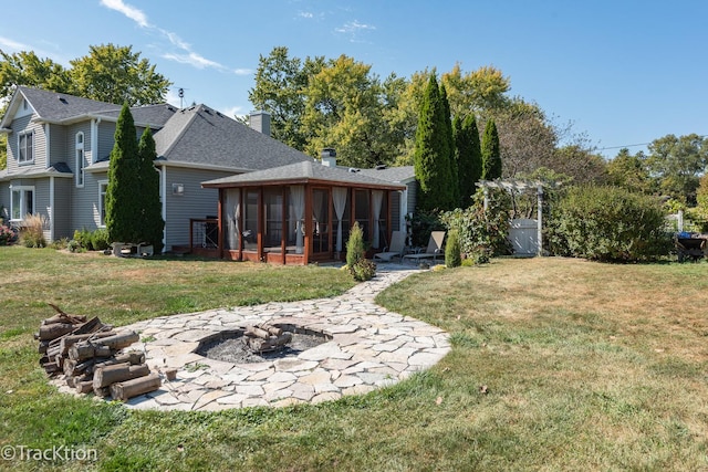 rear view of house with a patio, an outdoor fire pit, a lawn, and a sunroom