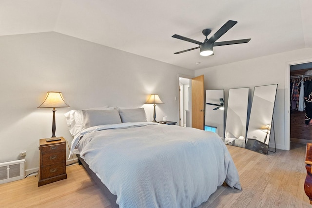 bedroom with ceiling fan, light hardwood / wood-style floors, vaulted ceiling, a walk in closet, and a closet