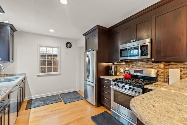 kitchen with light stone countertops, sink, light hardwood / wood-style floors, decorative backsplash, and appliances with stainless steel finishes