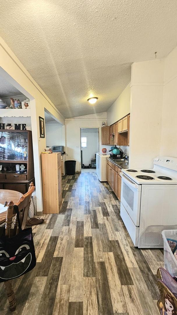 kitchen with white range with electric cooktop, vaulted ceiling, a textured ceiling, dark hardwood / wood-style flooring, and washer / clothes dryer