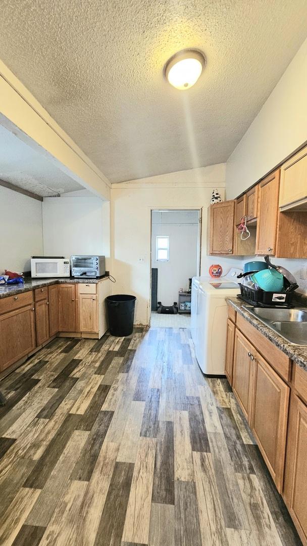 kitchen featuring washer / dryer, a textured ceiling, dark wood-type flooring, and sink