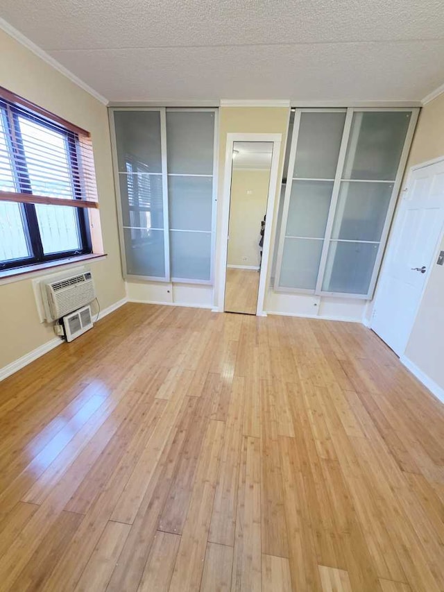 unfurnished bedroom with two closets, a wall mounted air conditioner, ornamental molding, hardwood / wood-style flooring, and a textured ceiling