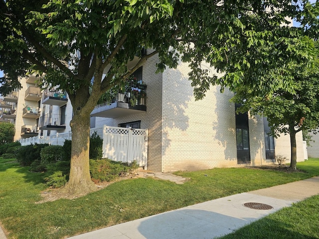 view of side of property with fence, a lawn, and brick siding