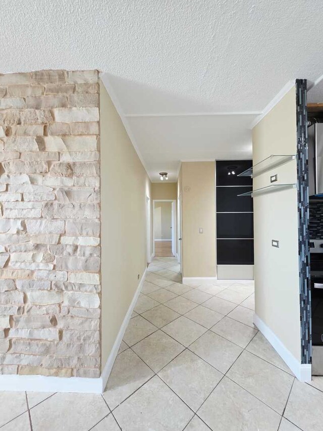 hallway featuring light tile patterned flooring, baseboards, and a textured ceiling