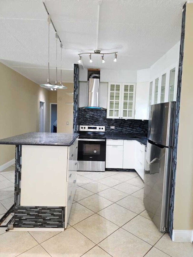 kitchen with light tile patterned floors, decorative backsplash, appliances with stainless steel finishes, dark countertops, and wall chimney exhaust hood