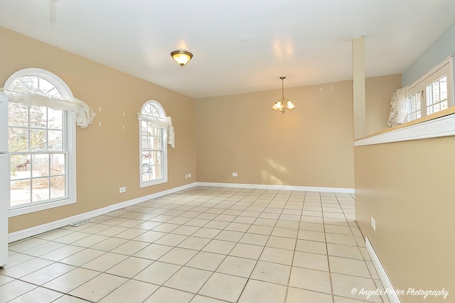 tiled spare room featuring a healthy amount of sunlight and an inviting chandelier