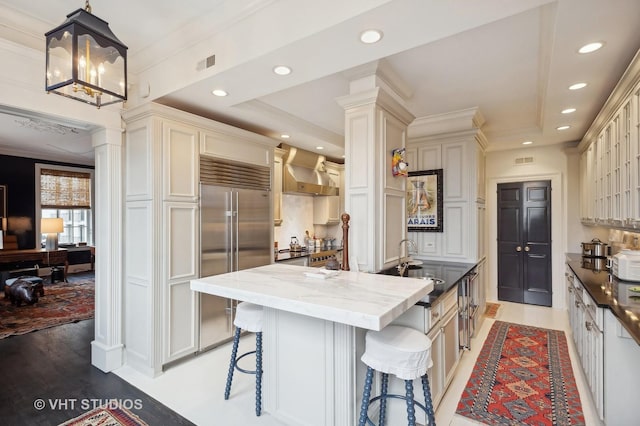 kitchen with pendant lighting, a breakfast bar, wall chimney range hood, sink, and built in refrigerator