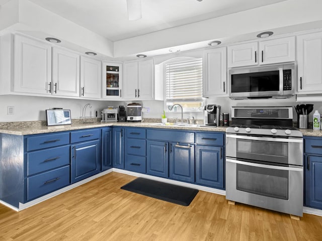 kitchen featuring light wood-type flooring, stainless steel appliances, sink, blue cabinetry, and white cabinets