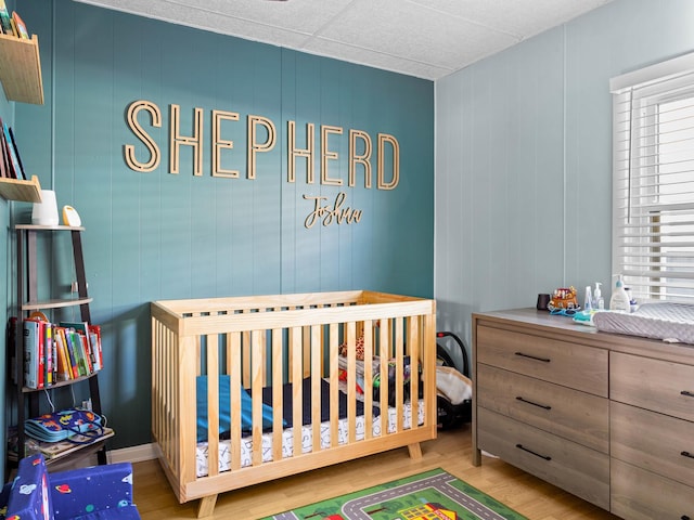 bedroom with light hardwood / wood-style floors, wooden walls, and a nursery area