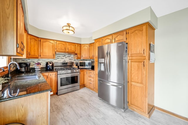 kitchen featuring sink, stainless steel appliances, tasteful backsplash, light hardwood / wood-style flooring, and dark stone countertops