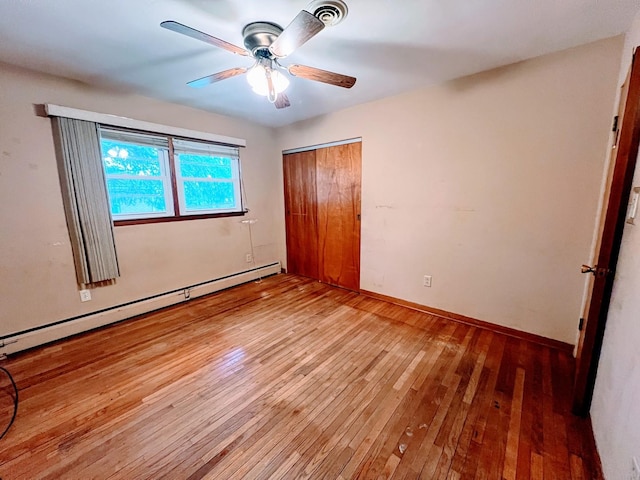 unfurnished bedroom featuring a closet, baseboard heating, hardwood / wood-style flooring, and ceiling fan