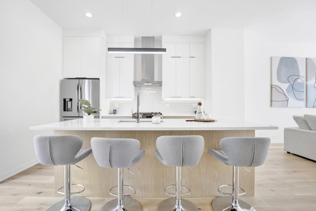 kitchen with white cabinetry, stainless steel fridge, and an island with sink