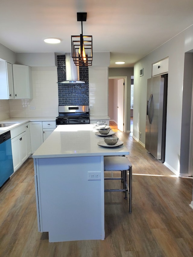 kitchen with white cabinetry, wall chimney exhaust hood, hanging light fixtures, a kitchen island, and appliances with stainless steel finishes