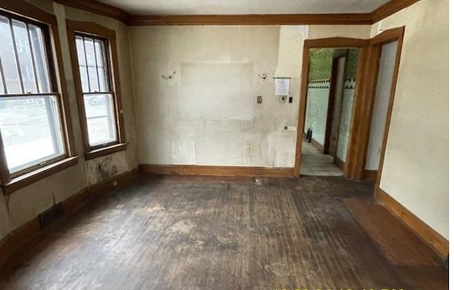 empty room with dark hardwood / wood-style flooring, crown molding, and a wealth of natural light