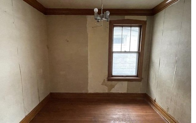 unfurnished room with hardwood / wood-style flooring, an inviting chandelier, and ornamental molding