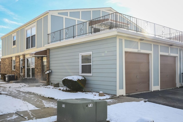 view of snowy exterior featuring central AC and a garage