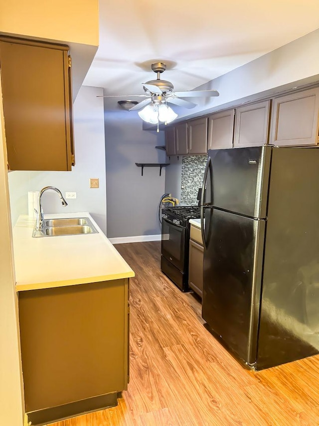 kitchen with black gas stove, sink, ceiling fan, fridge, and light hardwood / wood-style floors