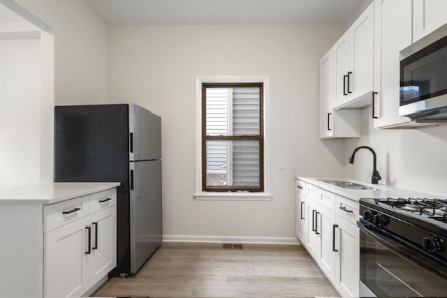 kitchen with sink, white cabinets, stainless steel appliances, and light wood-type flooring