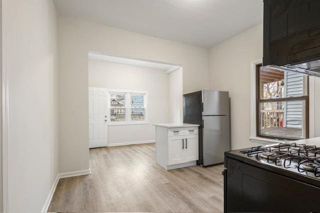 kitchen with stainless steel fridge, stove, white cabinetry, and light wood-type flooring