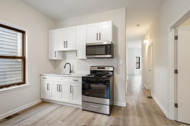 kitchen featuring appliances with stainless steel finishes, light wood-type flooring, white cabinetry, and sink