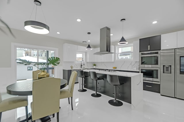 kitchen featuring decorative light fixtures, island exhaust hood, white cabinetry, and stainless steel appliances