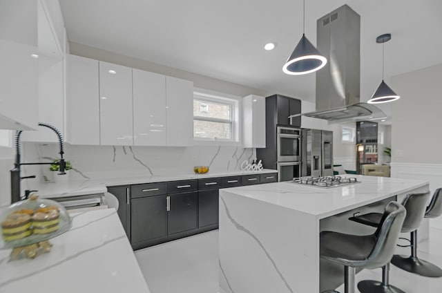 kitchen with white cabinetry, light stone counters, island exhaust hood, pendant lighting, and appliances with stainless steel finishes