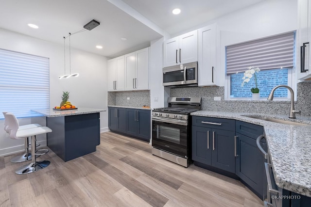 kitchen featuring white cabinetry, sink, hanging light fixtures, stainless steel appliances, and light stone counters