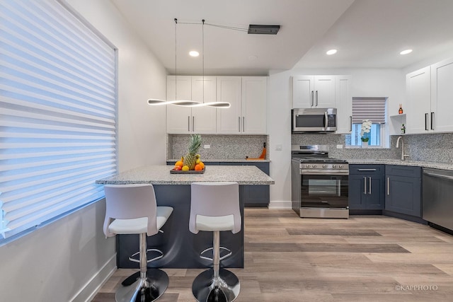 kitchen with white cabinetry, hanging light fixtures, stainless steel appliances, light stone counters, and a kitchen bar