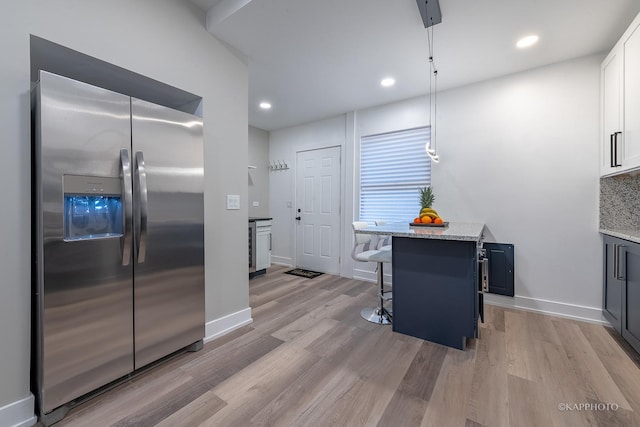 kitchen featuring white cabinetry, light stone countertops, stainless steel refrigerator with ice dispenser, decorative light fixtures, and a kitchen bar