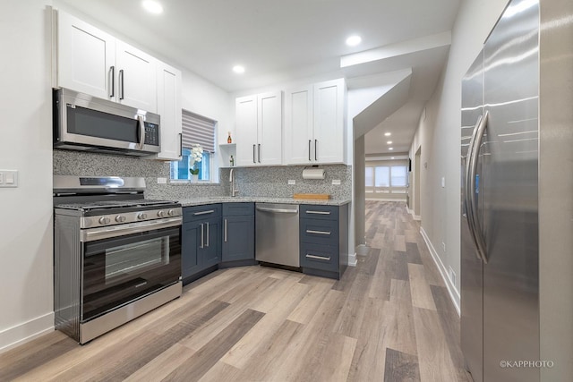 kitchen featuring sink, appliances with stainless steel finishes, decorative backsplash, white cabinets, and light wood-type flooring