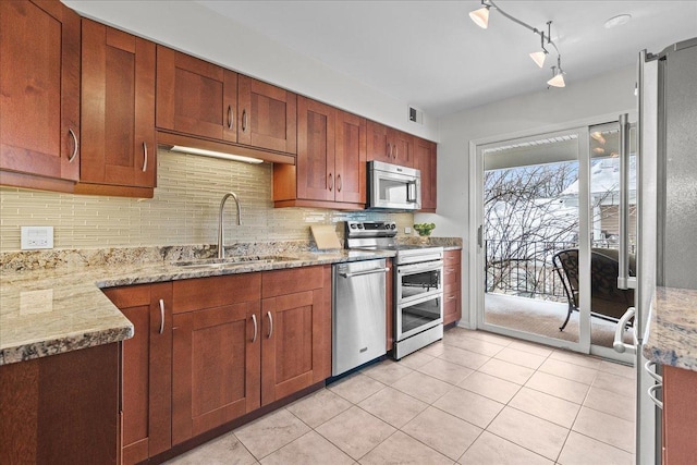 kitchen with appliances with stainless steel finishes, rail lighting, light stone counters, sink, and light tile patterned floors