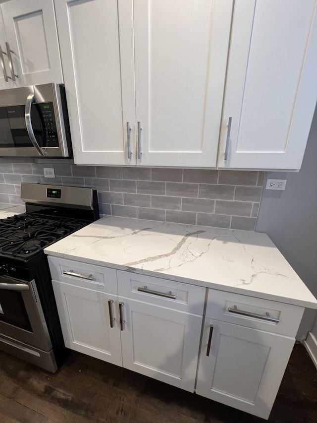 kitchen with appliances with stainless steel finishes, white cabinets, light stone countertops, and tasteful backsplash