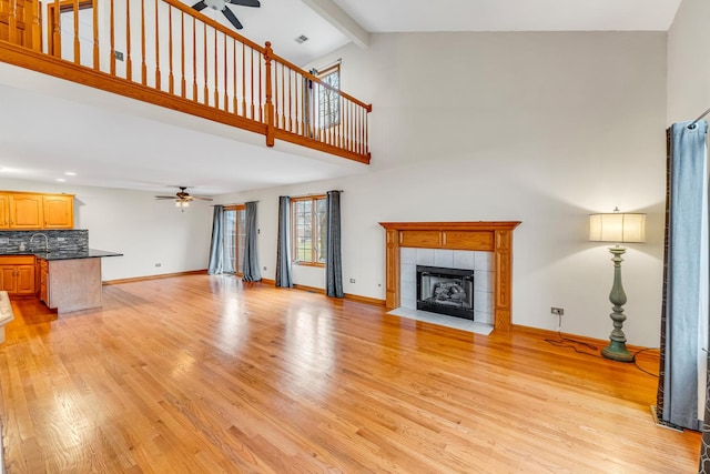 living room with beam ceiling, a tile fireplace, ceiling fan, high vaulted ceiling, and light wood-type flooring