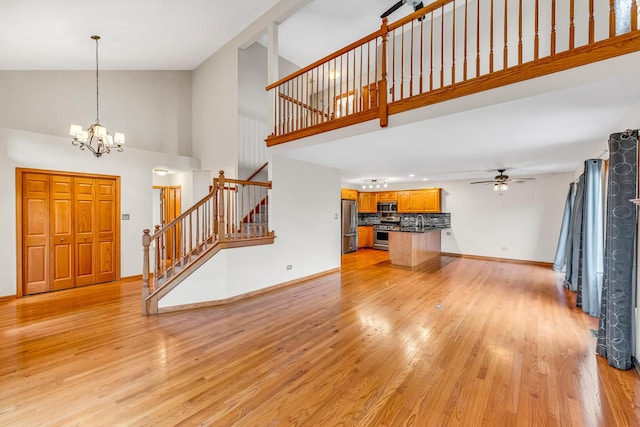 unfurnished living room with light hardwood / wood-style flooring, high vaulted ceiling, and ceiling fan with notable chandelier