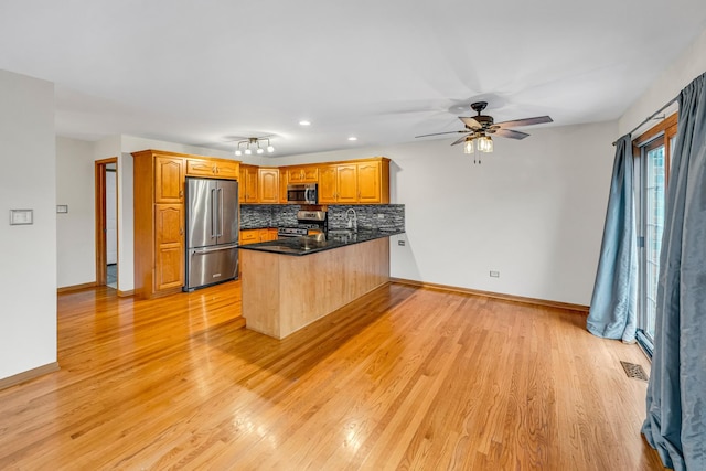 kitchen featuring kitchen peninsula, backsplash, stainless steel appliances, sink, and light hardwood / wood-style flooring